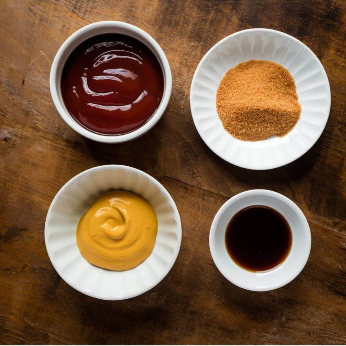 Chicken Meatloaf Recipe glaze ingredients, including ketchup, mustard, brown sugar, and Worcestershire sauce, arranged in white bowls on a rustic wooden surface. A tangy and flavorful topping for a juicy meatloaf.