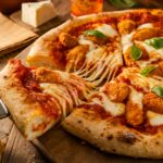 A homemade Chicken Parm Pizza with a golden-brown crust, crispy breaded chicken pieces, gooey melted mozzarella, and rich marinara sauce. A slice is being pulled, stretching the cheese. Fresh basil leaves add a pop of color, and the pizza sits on a rustic wooden board with a cozy, warm background.