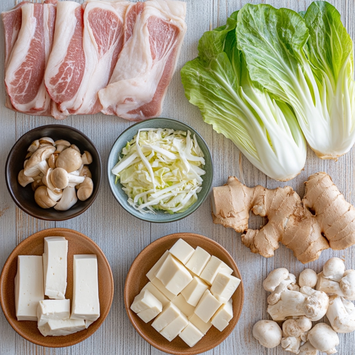 An overhead image of Mille Feuille Nabe ingredients, including sliced pork belly, bok choy, shredded cabbage, white mushrooms, enoki mushrooms, tofu cubes, and fresh ginger. The ingredients are neatly arranged on a wooden surface with soft lighting highlighting their freshness.