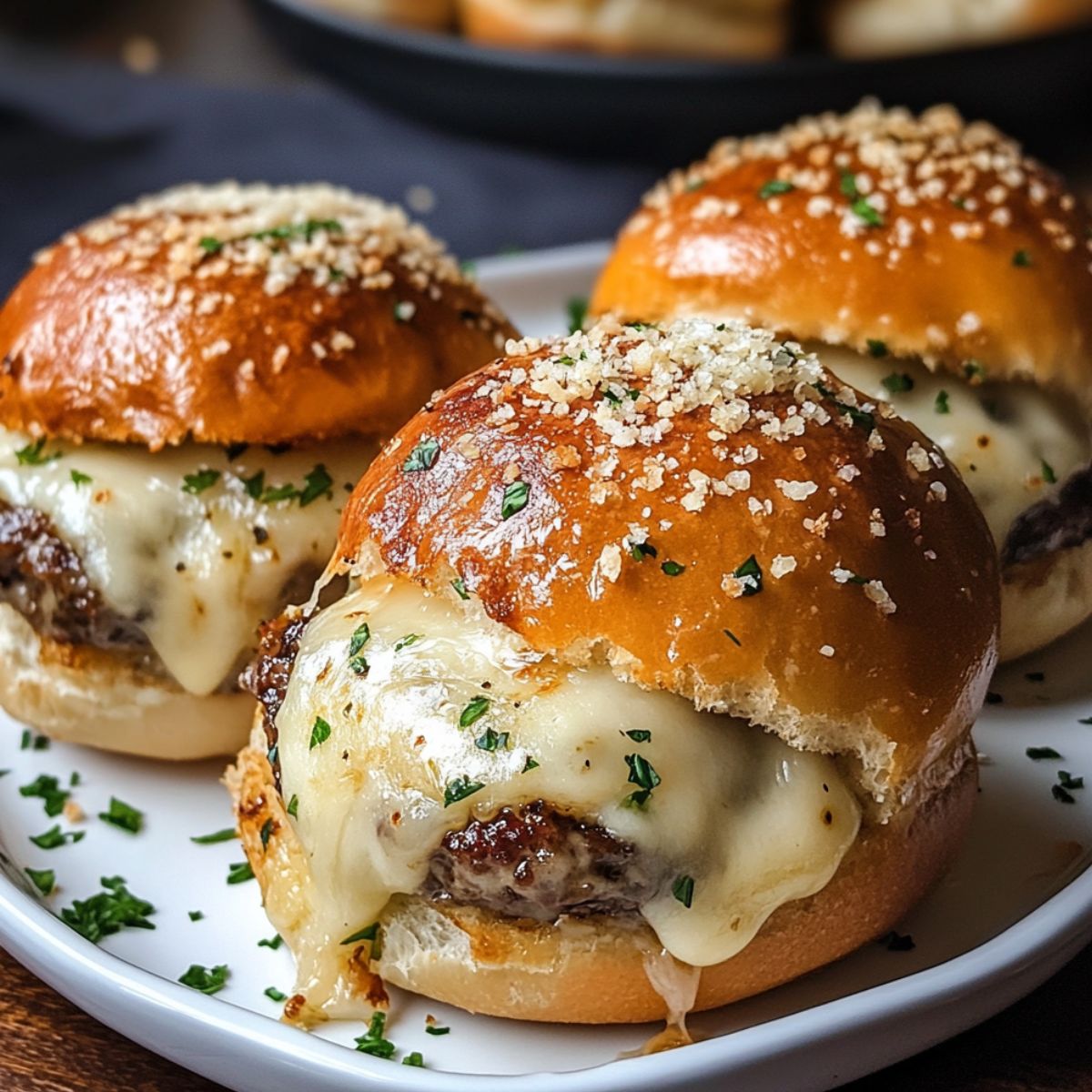 Homemade garlic parmesan cheeseburger bombs with melted cheese, golden buns, and a sprinkle of herbs, served on a white plate.