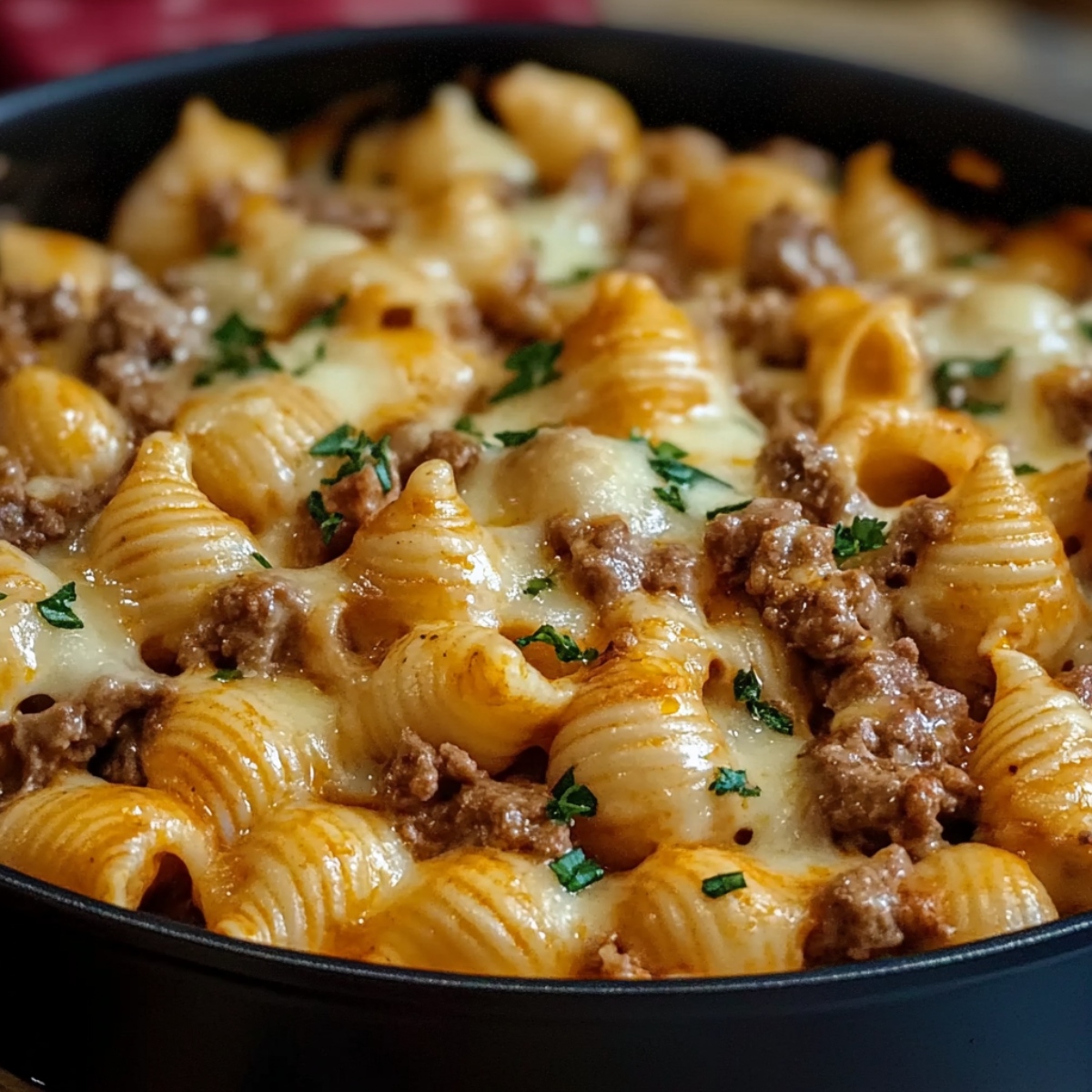 Homemade creamy beef and shells pasta with melted cheese, ground beef, and fresh parsley in a skillet.