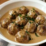 Homemade Swedish meatballs in creamy brown gravy, topped with fresh parsley, served in a white bowl.