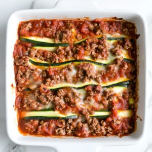 Zucchini lasagna in a white baking dish with meat sauce, melted cheese, and visible zucchini layers.