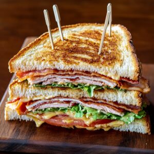 Triple-decker homemade club sandwich with turkey, bacon, lettuce, tomato, and mayo, secured with toothpicks and stacked on a wooden board.
