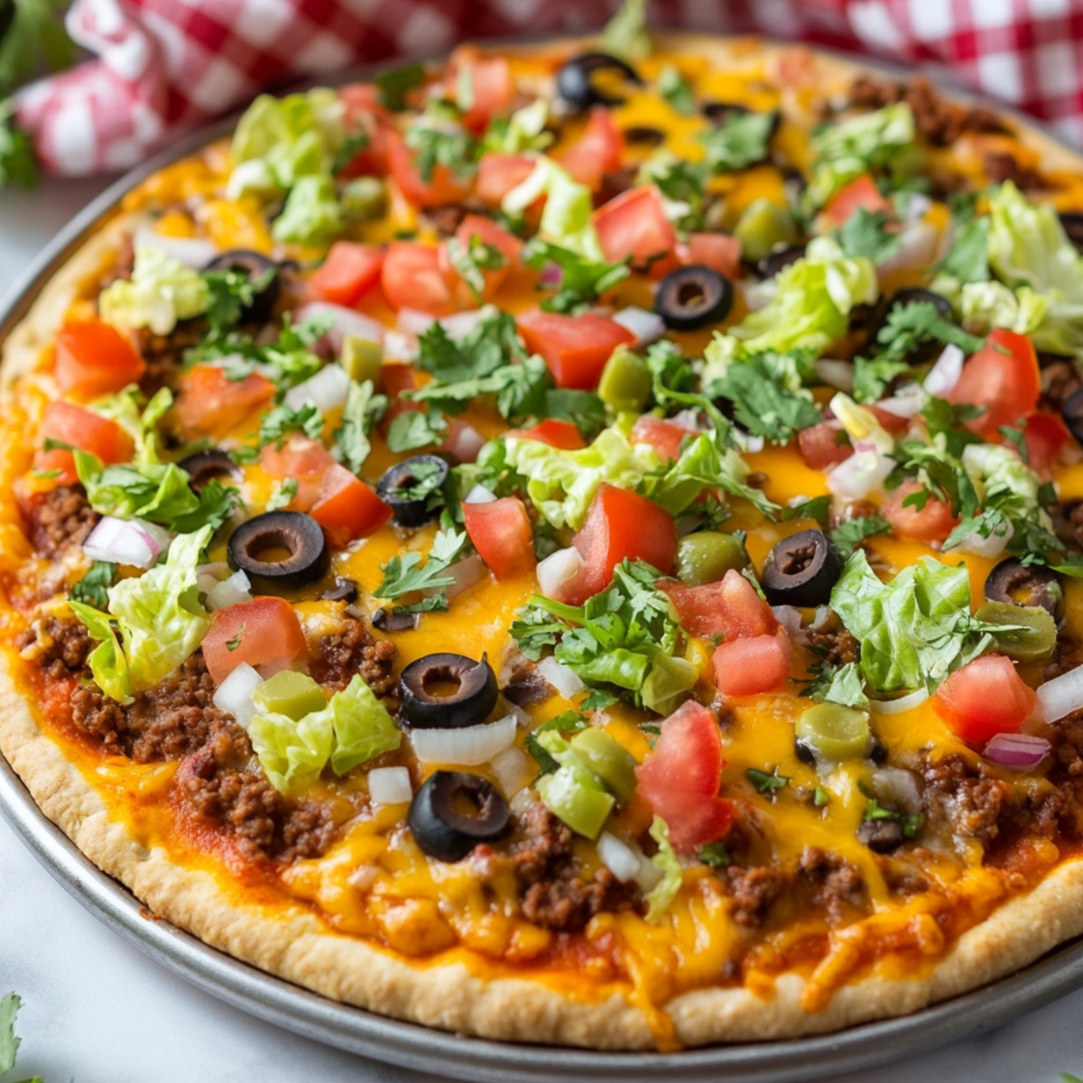 Homemade taco pizza topped with melted cheese, seasoned beef, shredded lettuce, diced tomatoes, black olives, onions, green olives, and fresh cilantro.
