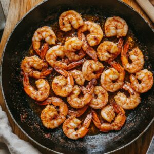 Seasoned shrimp cooking in a hot skillet with golden oil and crisp edges, perfectly seared for homemade shrimp tacos.