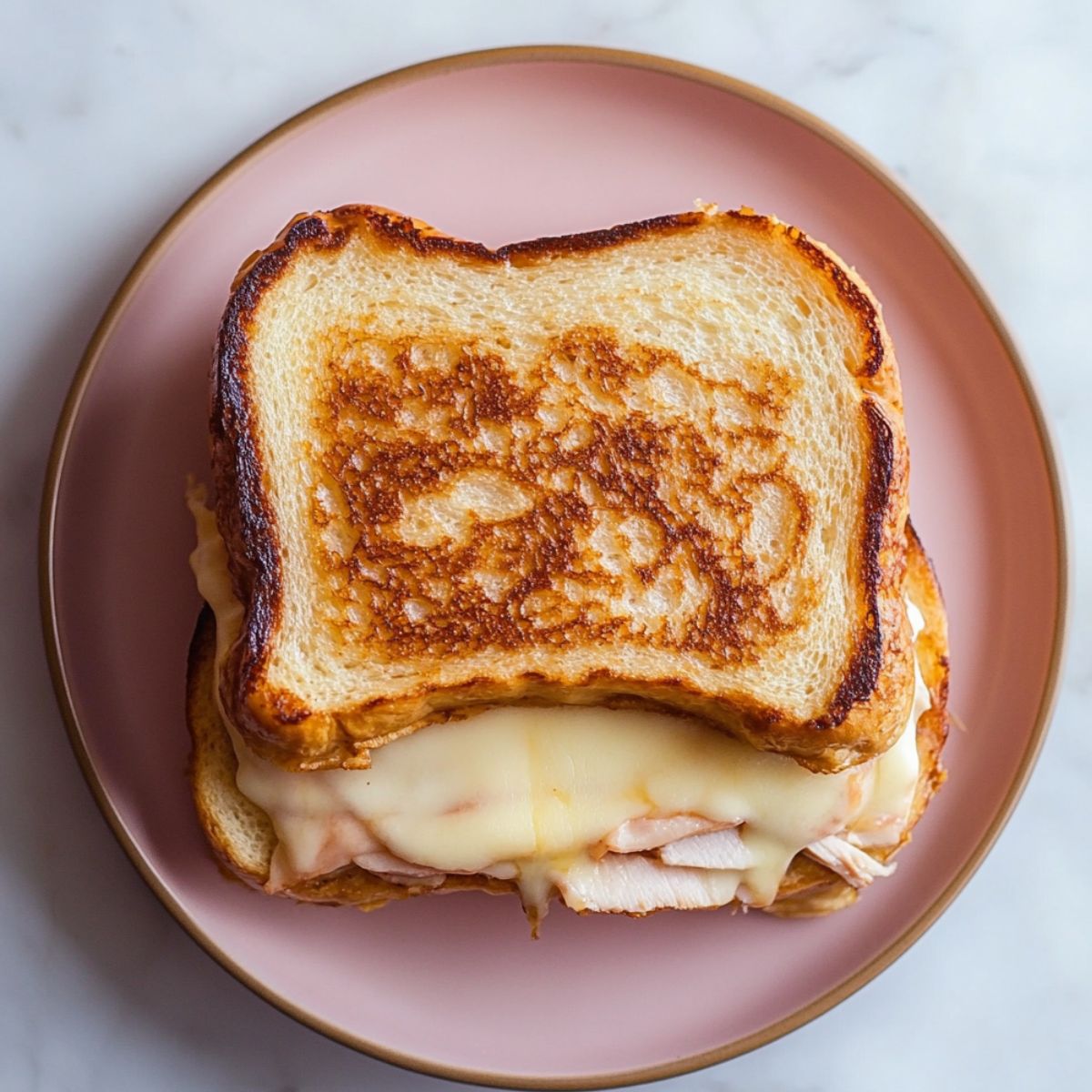 A golden-brown Monte Cristo sandwich with melted cheese and turkey, served on a pink plate with a gold rim, ready to eat.