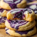 Close-up of homemade blueberry cheesecake swirl cookies with golden edges and rich purple blueberry filling, one cookie partially bitten to reveal a soft, moist center.