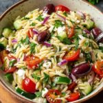 Homemade Greek orzo salad with cherry tomatoes, cucumber, red onion, Kalamata olives, feta cheese, and parsley in a rustic bowl, lightly dressed with olive oil.