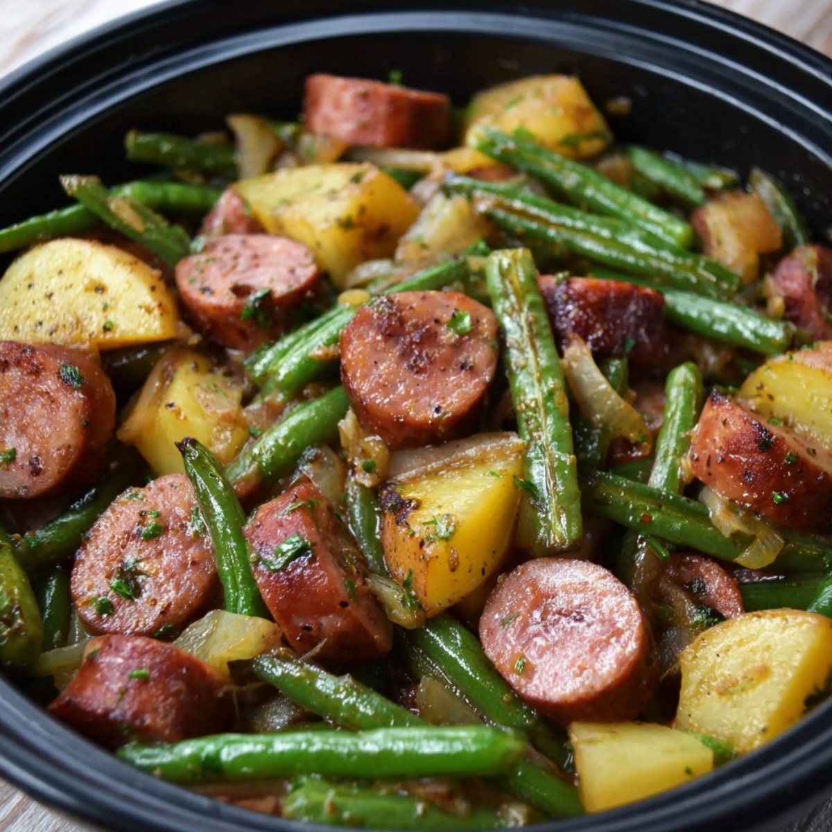 A homemade Kielbasa Green Beans and Potatoes, baby potatoes, and green beans, cooked with onions and herbs, served in a black slow cooker.