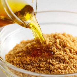 Melted butter being poured into a bowl of crushed Biscoff cookies, captured up close with a warm, natural light for a homemade look.