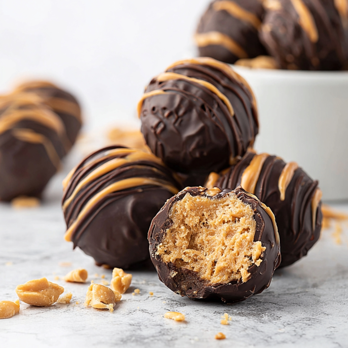 Homemade chocolate-coated peanut butter balls on a wooden board, topped with crushed peanuts, with one ball bitten to show a creamy, textured peanut butter filling.