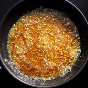 Golden honey butter sauce bubbling in a black skillet with minced garlic floating in the glossy mixture, captured during cooking on the stovetop.