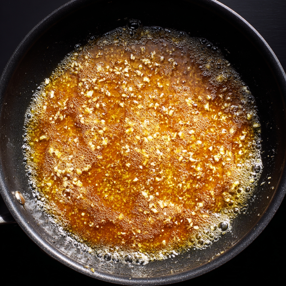 Golden honey butter sauce bubbling in a black skillet with minced garlic floating in the glossy mixture, captured during cooking on the stovetop.