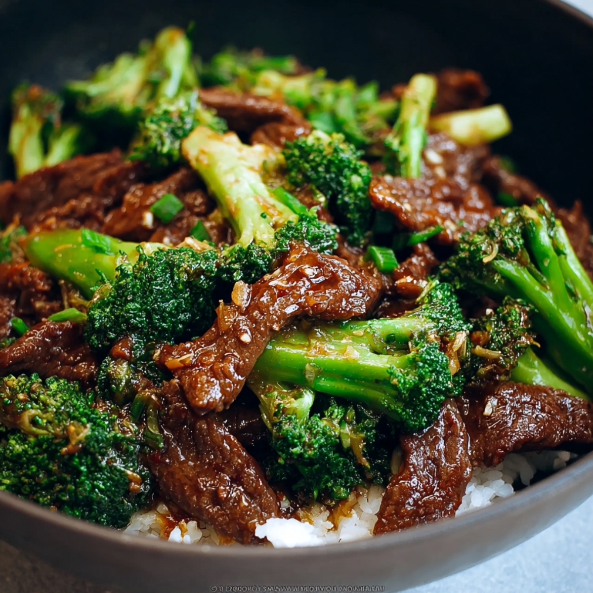 Close-up of homemade Chinese beef and broccoli in a dark pan, tender beef in glossy brown sauce with vibrant broccoli and sesame seeds, natural daylight.
