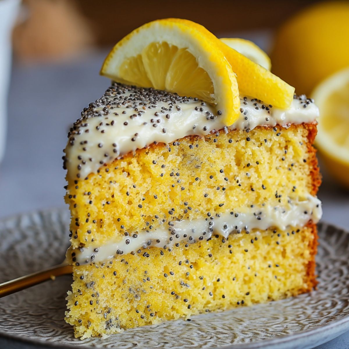 Homemade Lemon Poppyseed Cake with lemon frosting, poppy seed topping, and lemon wedge garnish on a textured plate with a gold fork.