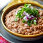 Homemade refried beans in a bowl topped with fresh cilantro and red onion