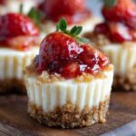 Homemade Strawberry Cheesecake Bites with crumbly graham cracker crust, creamy filling, and glossy strawberry topping with a whole strawberry piece on top, on a wooden board.