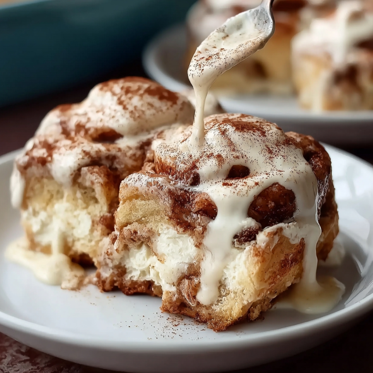 Close-up of Tres Leches Cinnamon Rolls on a white plate, drizzled with creamy sauce and dusted with cinnamon.