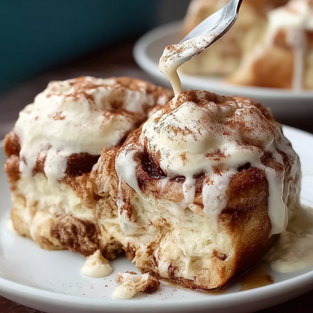 Tres Leches Cinnamon Rolls on a white plate, topped with creamy sauce and dusted with cinnamon.