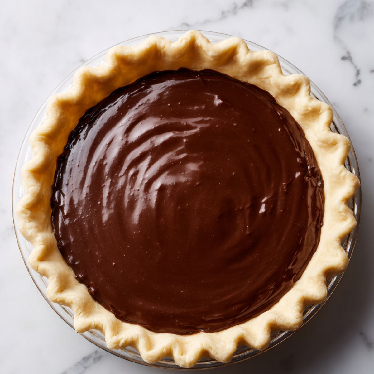 A homemade Hot Fudge Pie with a golden, crimped crust and a smooth, glossy chocolate filling. The rich, velvety filling has a slight sheen, sitting perfectly within the rustic crust on a marble surface.