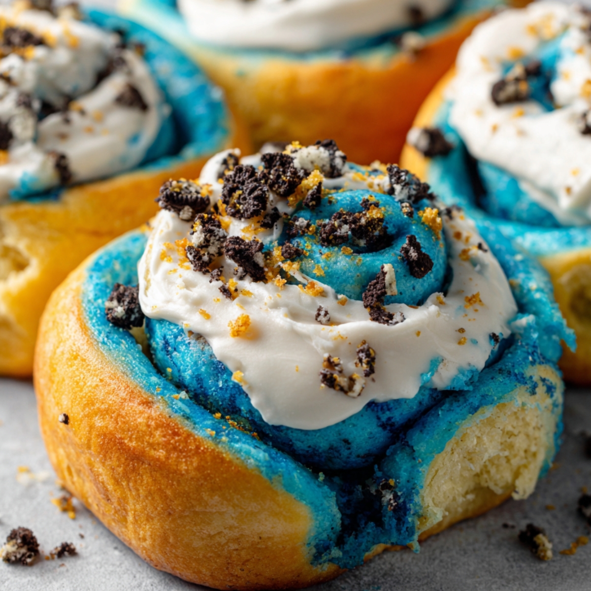 Cookie Monster Cinnamon Rolls with golden edges, blue swirled dough, cream cheese frosting, and Oreo crumbles.