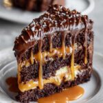 Easy Chocolate Caramel Cake Recipe layered with gooey caramel, topped with glossy ganache and sea salt on a white plate.