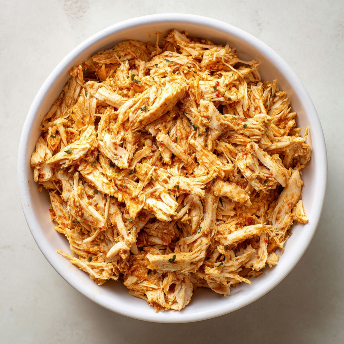 Seasoned shredded chicken filling in a white bowl, coated with spices and herbs, ready to be used for homemade chicken flautas.