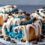 Homemade Cookie Monster cinnamon rolls with blue swirled dough, white icing drizzle, Oreo crumbles, and golden edges.