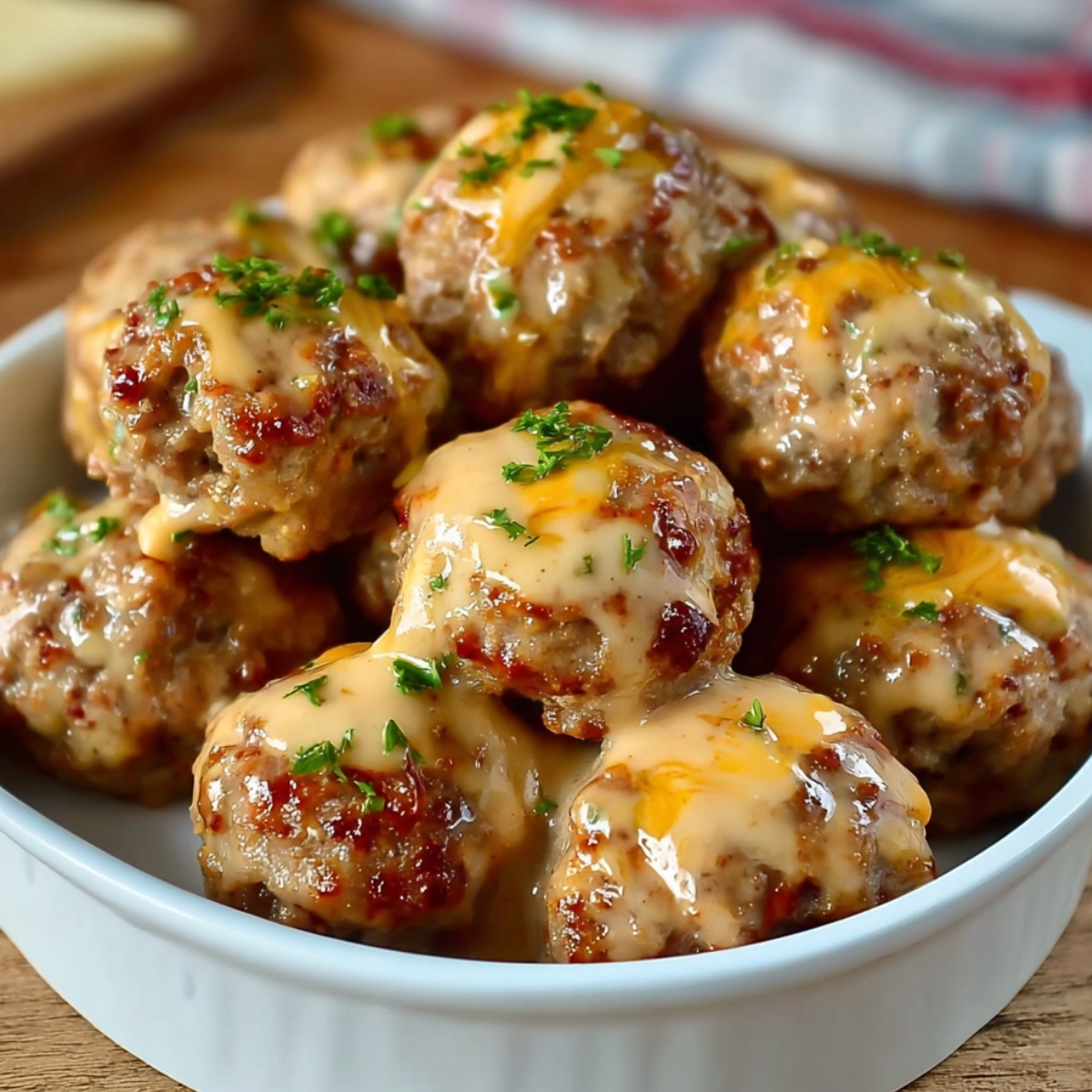 Homemade Rotel Cream Cheese Sausage Balls stacked in a white dish on a wooden board, golden brown with melted cheddar and parsley, dipping sauce in background.