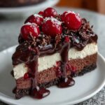 A slice of homemade Black Forest Cheesecake with chocolate and vanilla layers on a cookie crust, topped with glossy ganache, fresh cherries, chocolate shavings, and cherry filling dripping down the sides.