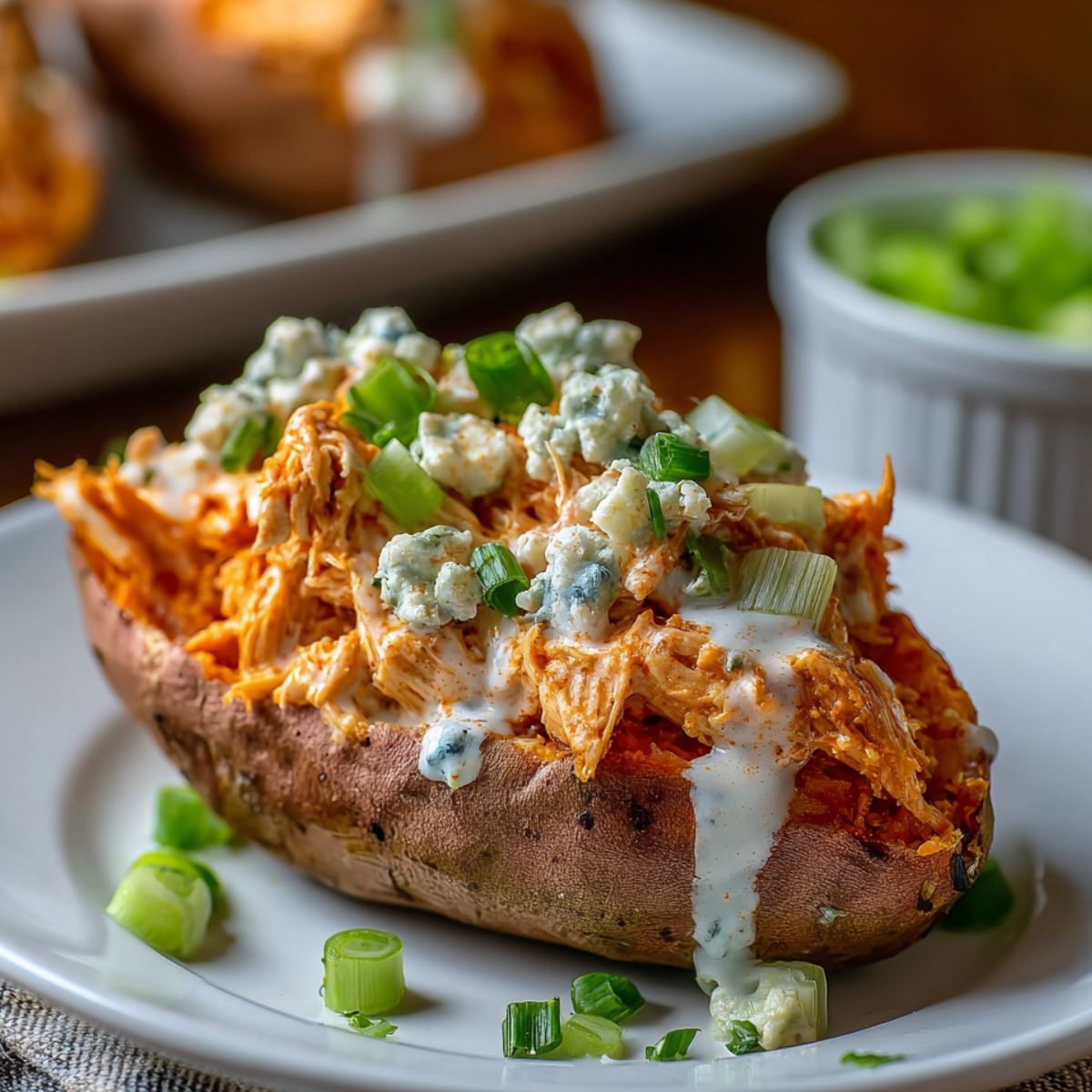 Buffalo Chicken Stuffed Sweet Potatoes topped with ranch, blue cheese, and green onions on a white plate, warm natural light, homemade and fresh.