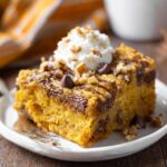 Homemade Pumpkin Earthquake Cake with whipped cream, chocolate chips, pecans, and caramel drizzle on a white plate.