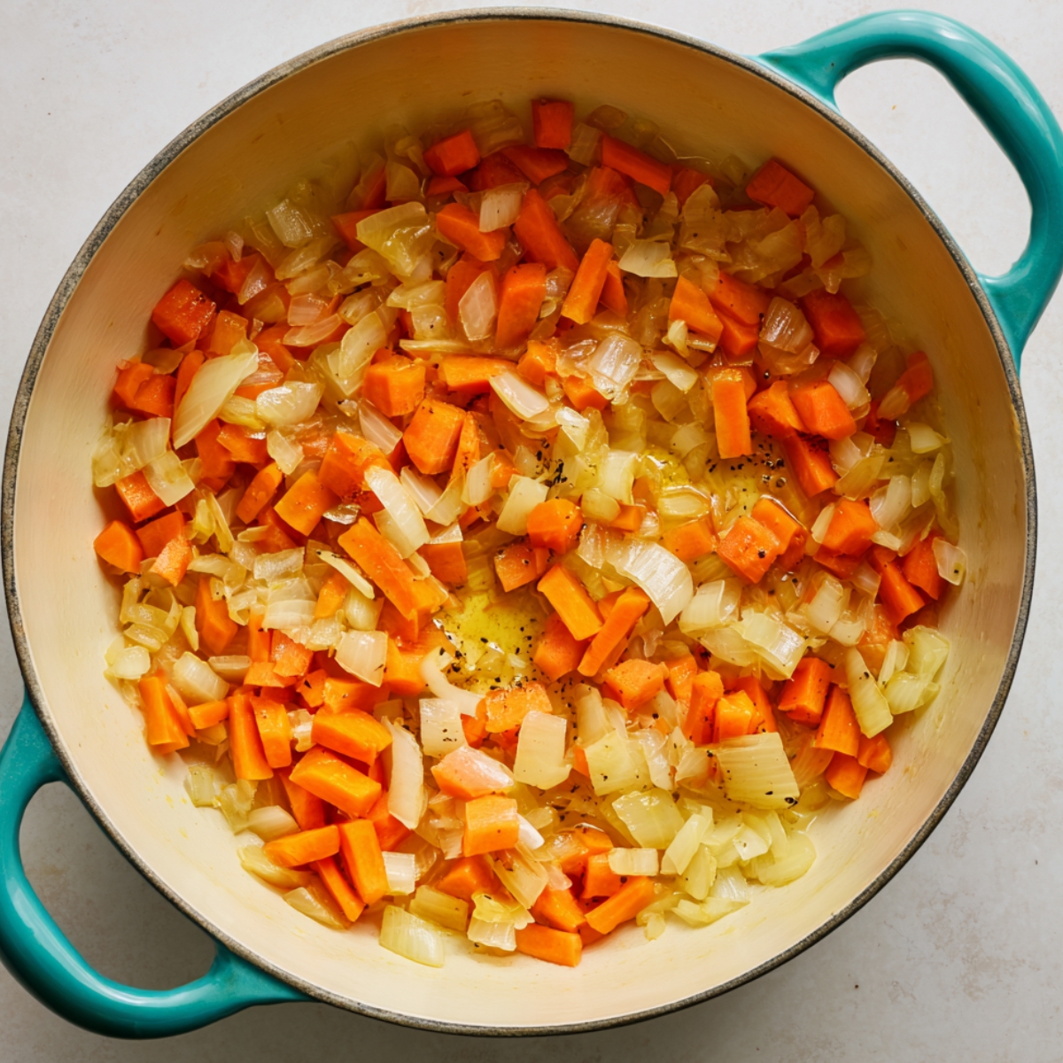 Sautéed carrots and onions in a cream-colored Dutch oven with teal handles, forming the flavor base for homemade Bisquick chicken and dumplings.