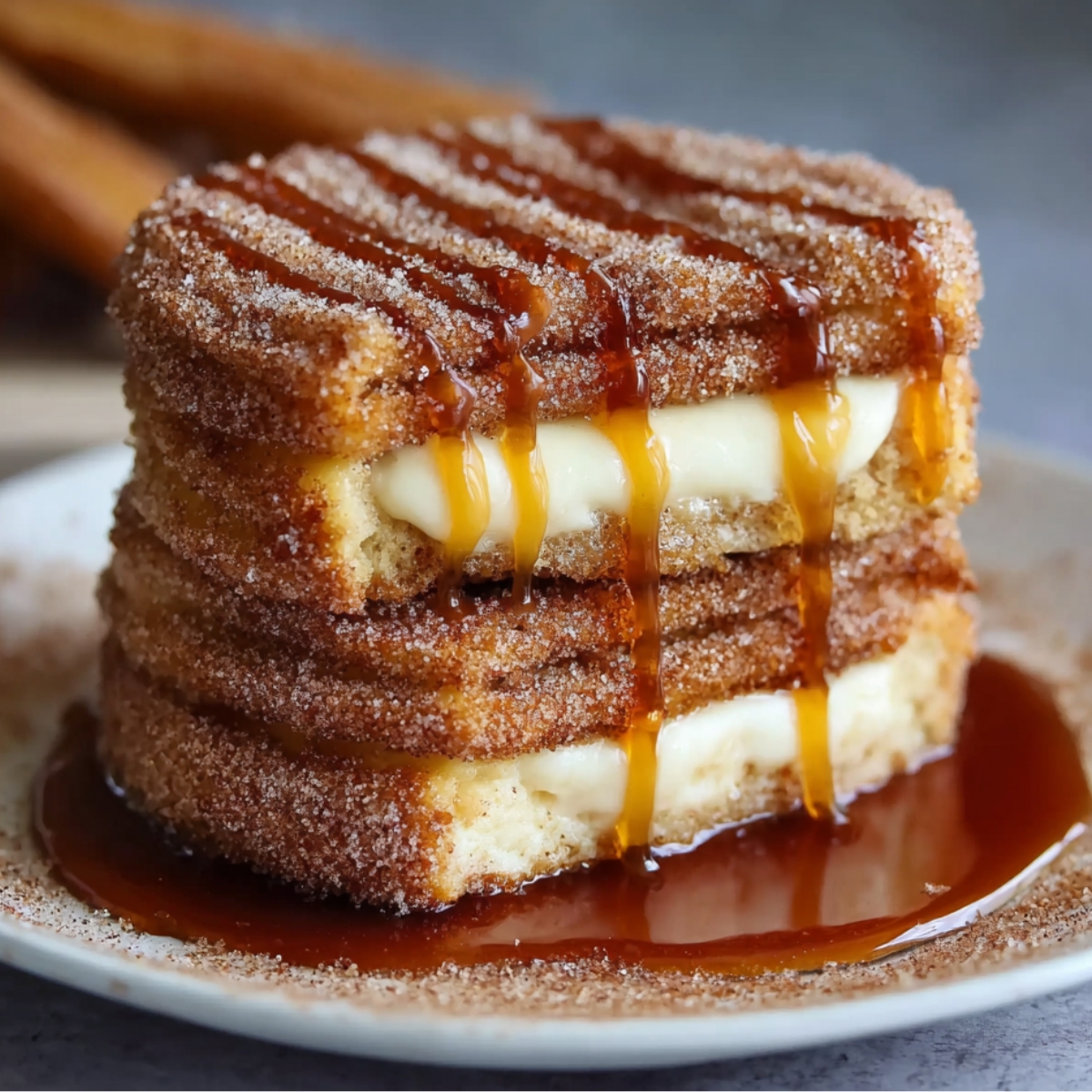 Churro Cheesecake served on a plate, coated in cinnamon sugar, layered with creamy cheesecake filling, and drizzled generously with caramel sauce.