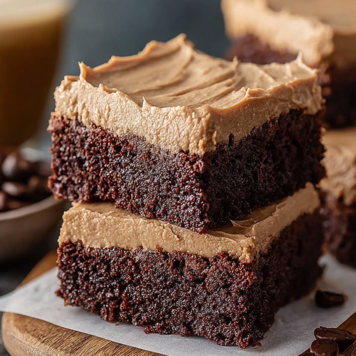 Homemade Frosted Coffee Brownies stacked on parchment paper, showing a dense, fudgy chocolate base and thick, creamy coffee buttercream frosting on top, with soft texture and natural crumbs visible, set on a wooden board for a cozy, real kitchen look.
