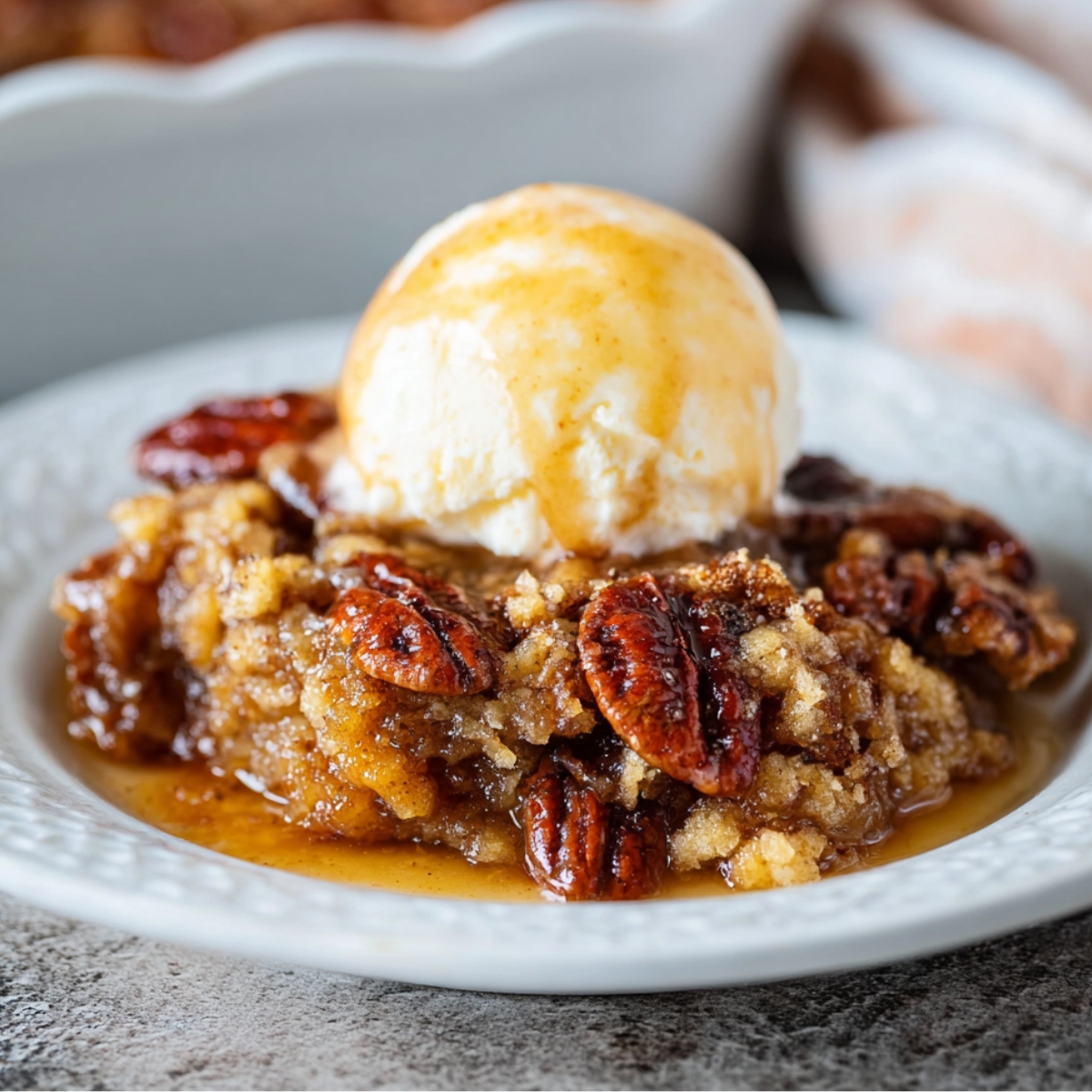 Homemade Pecan Pie Cobbler topped with a scoop of melting vanilla ice cream, featuring caramelized pecans and a gooey brown sugar filling on a white dessert plate.