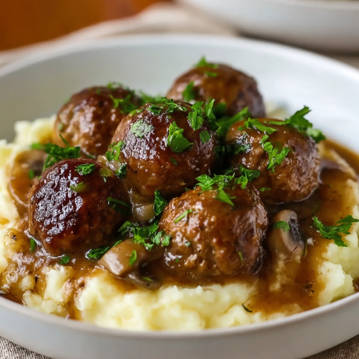 Salisbury steak meatballs served over creamy mashed potatoes with rich onion gravy and fresh parsley on top.