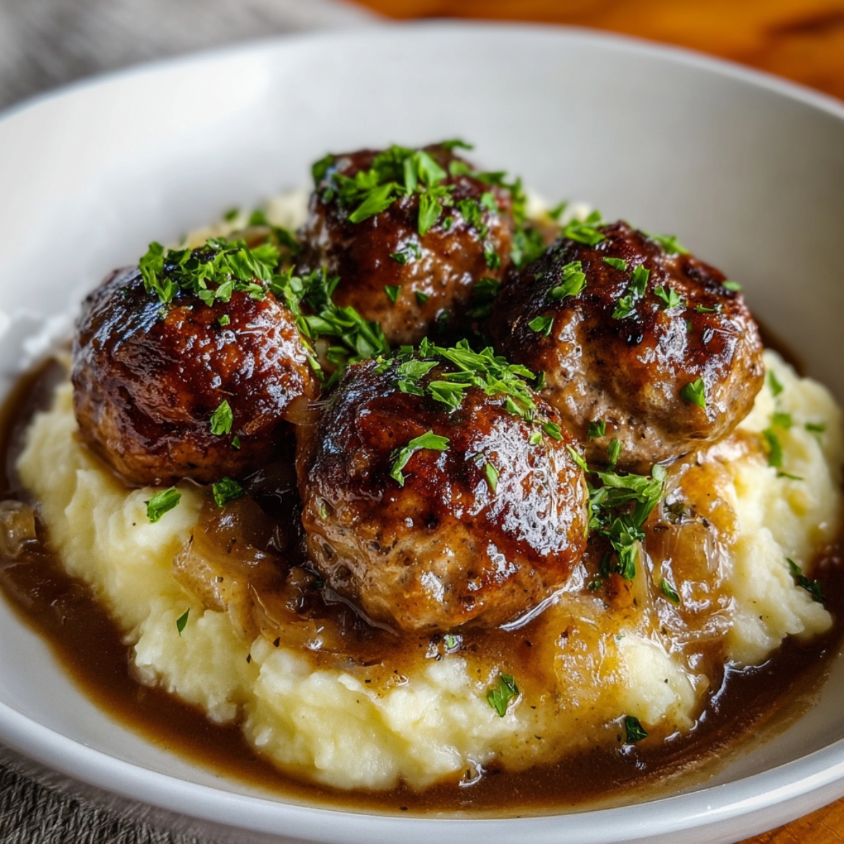 Homemade Salisbury steak meatballs served over creamy mashed potatoes with rich onion gravy and fresh parsley on top.