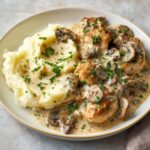 A plate of creamy chicken stroganoff with sautéed mushrooms, served alongside mashed potatoes, garnished with fresh parsley.