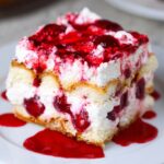 Homemade Cherry Amaretto Tiramisu with whipped cream, cherries, and cherry syrup on top, served on a white plate.