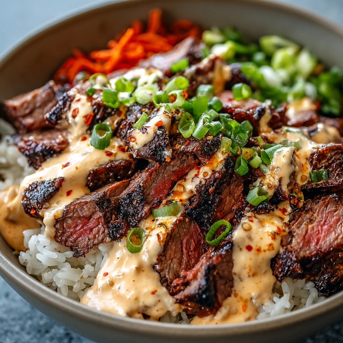 Homemade Korean BBQ Steak Bowls with sliced grilled steak, rice, spicy mayo, scallions, carrots, and greens.