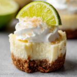 Mini Margarita Cheesecakes topped with whipped cream and a slice of lime, showcasing a smooth, creamy texture with a graham cracker crust.