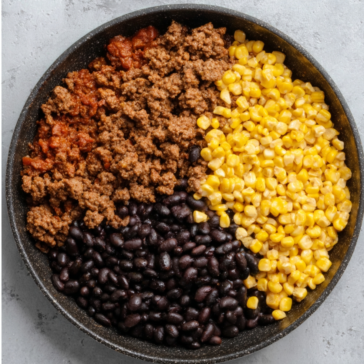 A skillet filled with seasoned ground beef, black beans, corn, and spices, mixed together for bell pepper stuffing.
