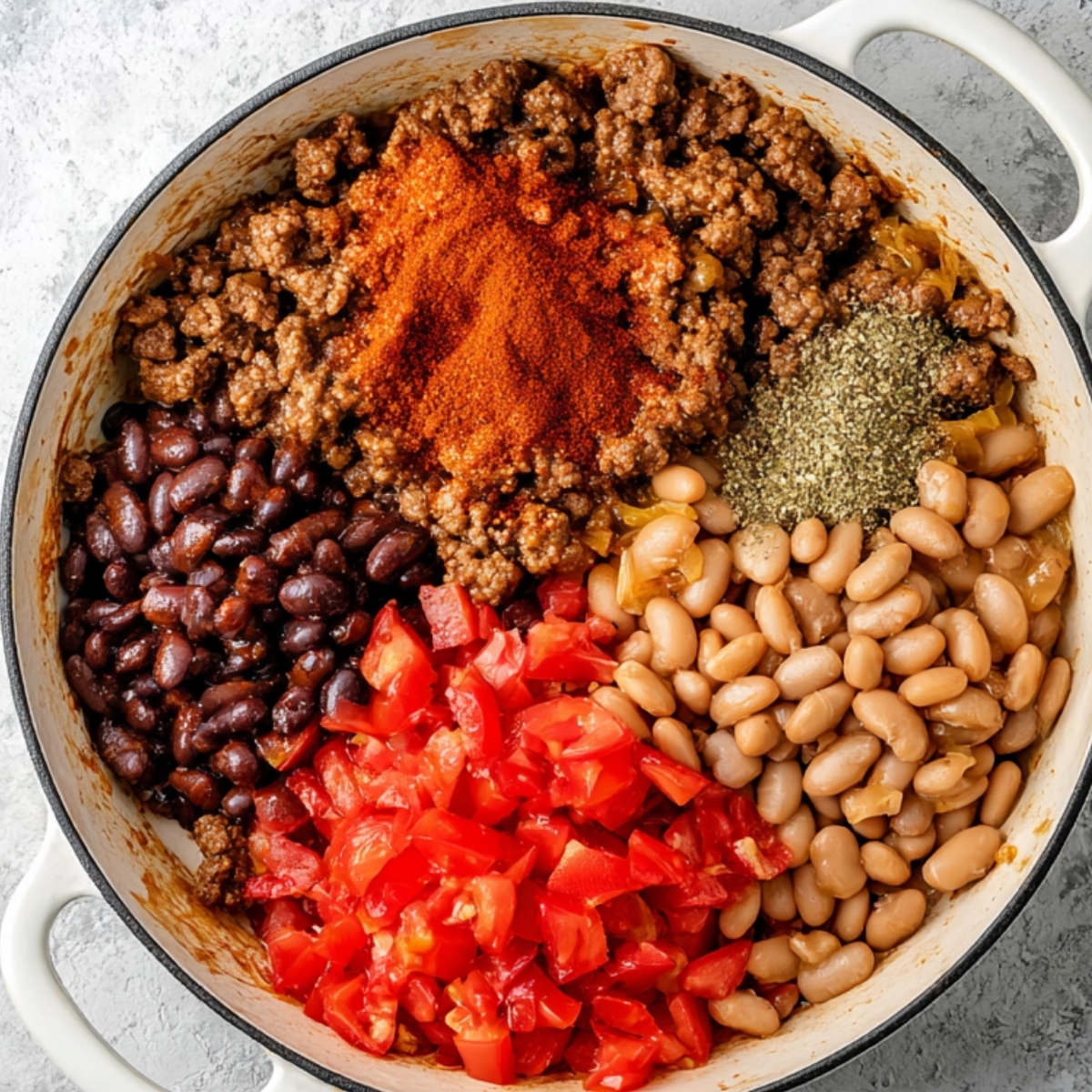 Skillet filled with cooked ground beef, black beans, pinto beans, diced tomatoes, and taco seasoning before stirring