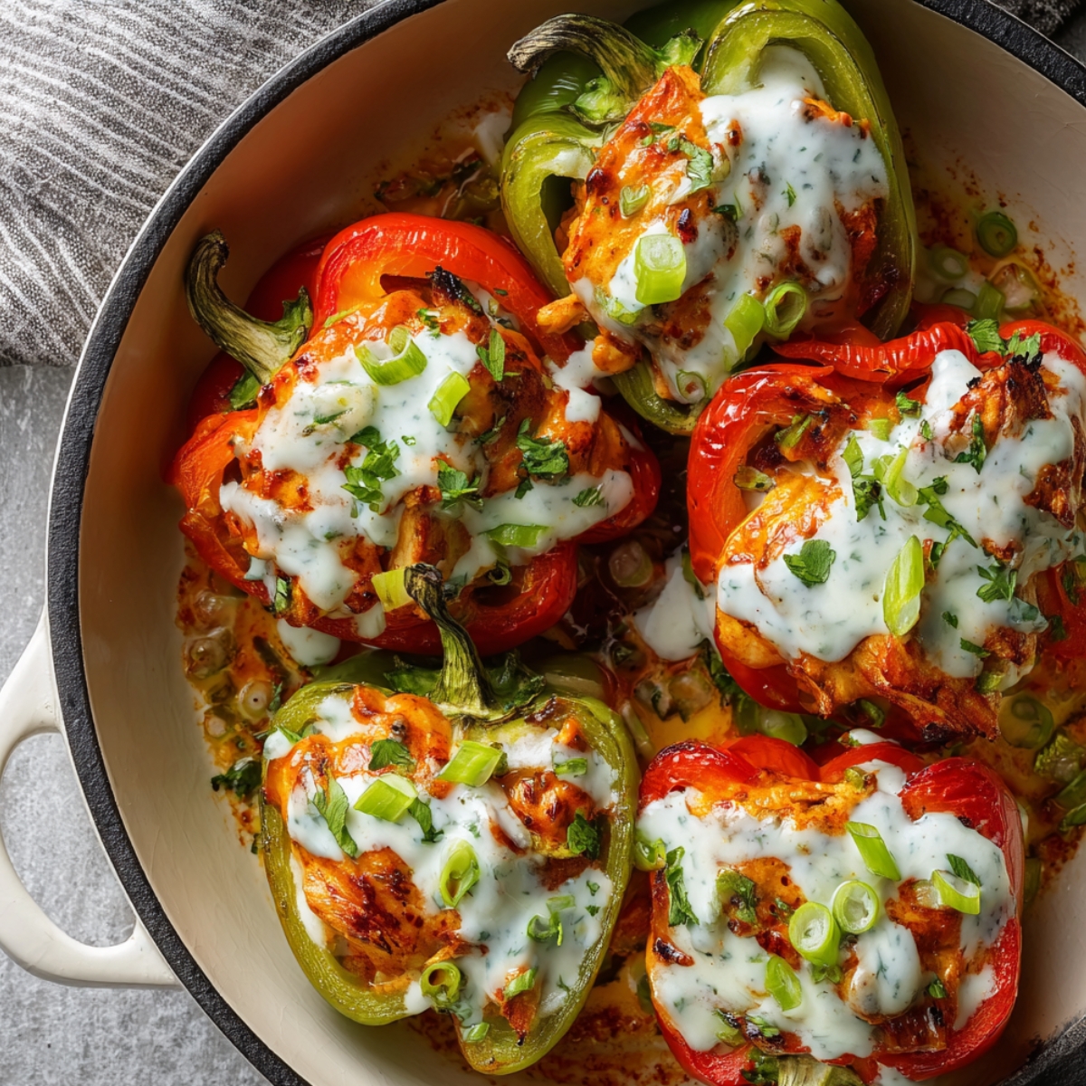 Close-up view of roasted red and green Buffalo Chicken Stuffed Peppers Recipe, drizzled with creamy sauce and garnished with sliced green onions and herbs, showing melted, slightly charred edges.