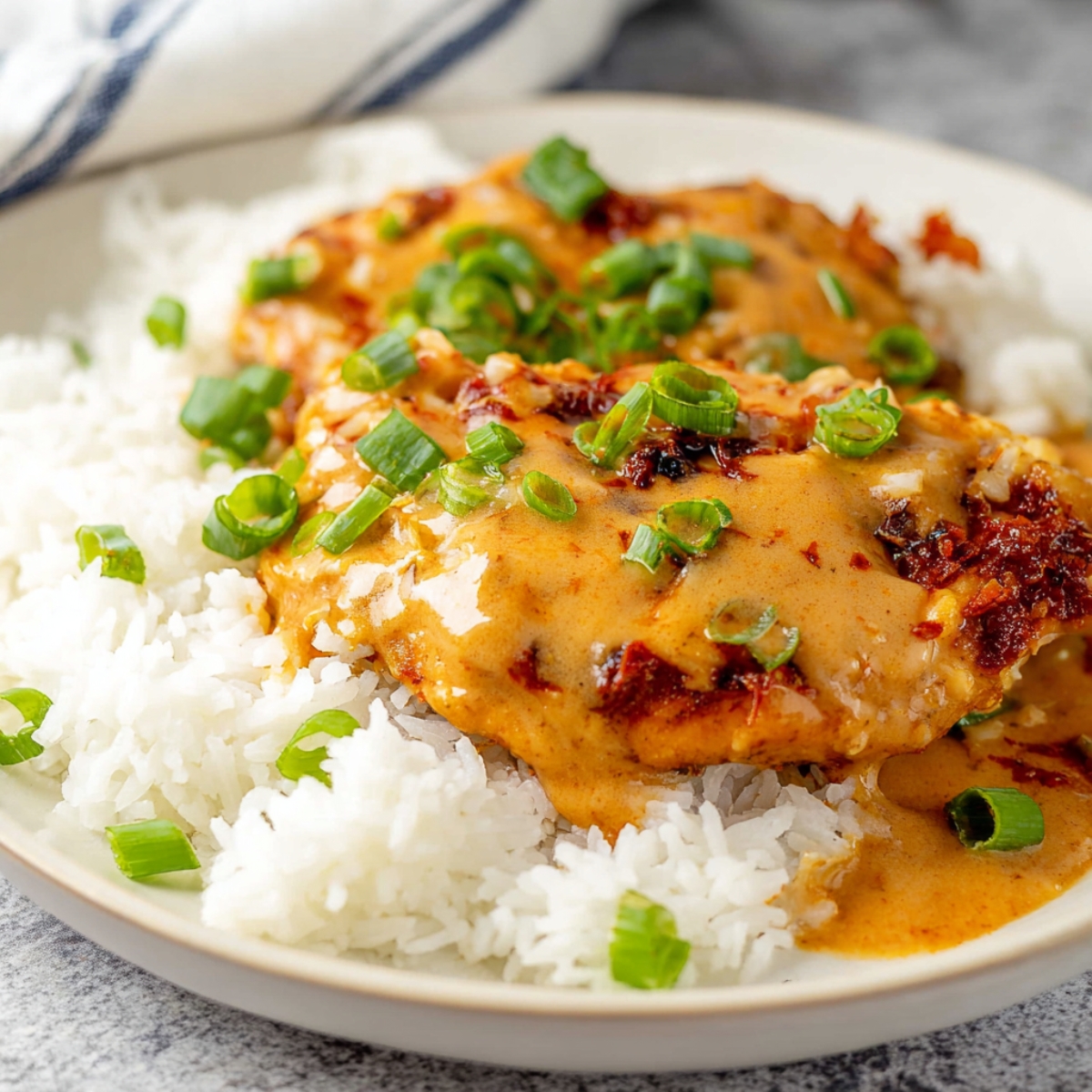 Chicken Diablo with creamy sauce, topped with chopped green onions, served over a bed of white rice.