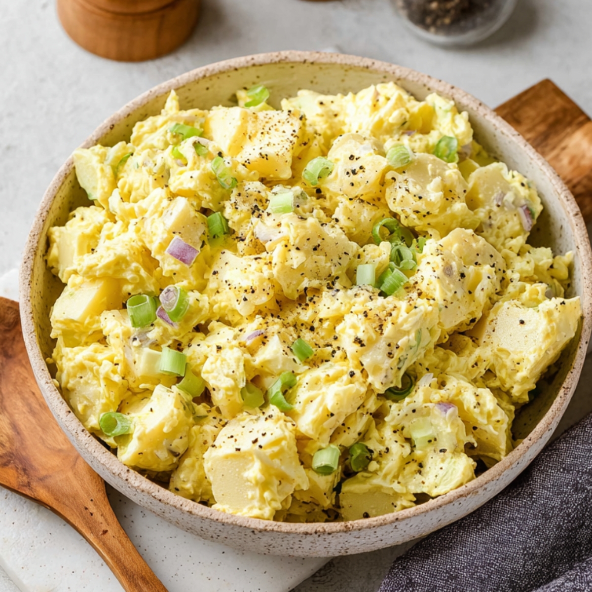 A creamy and freshly made classic potato salad, garnished with freshly ground black pepper and served in a light gray bowl.
