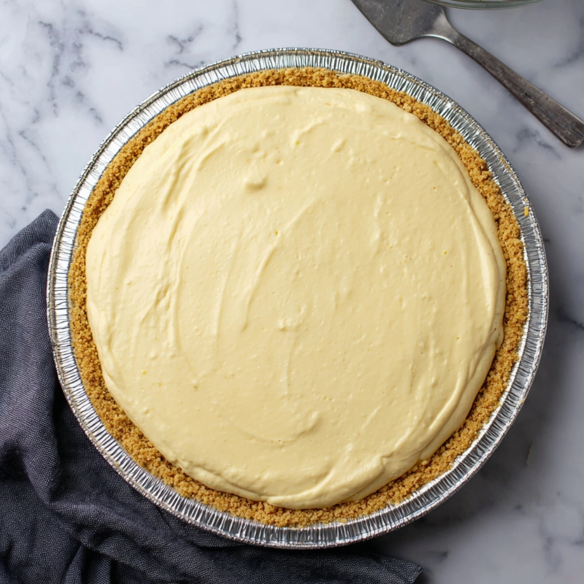 Whole no-bake eggnog pie in graham cracker crust before chilling on marble surface