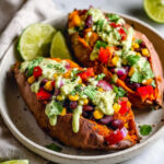 Healthy Mexican Stuffed Sweet Potatoes filled with black beans, corn, peppers, and drizzled with creamy avocado sauce in a rustic bowl.